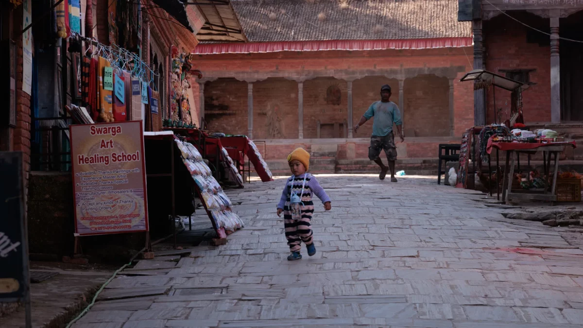 Baby running in the street of Changunarayan right in front of a Thangka mandala school, Nepal