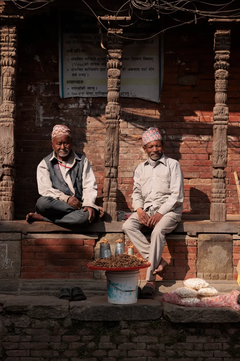 two men sitting in front of an old house in bhaktapur durbar square, nepal