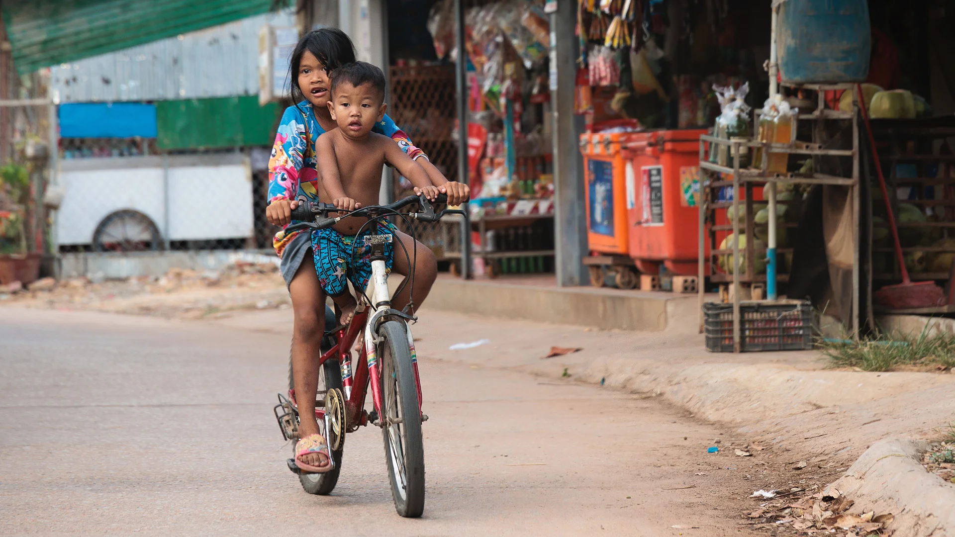 Brother and sister playing on bicycle in a dusty neighbourhood in Siem Reap