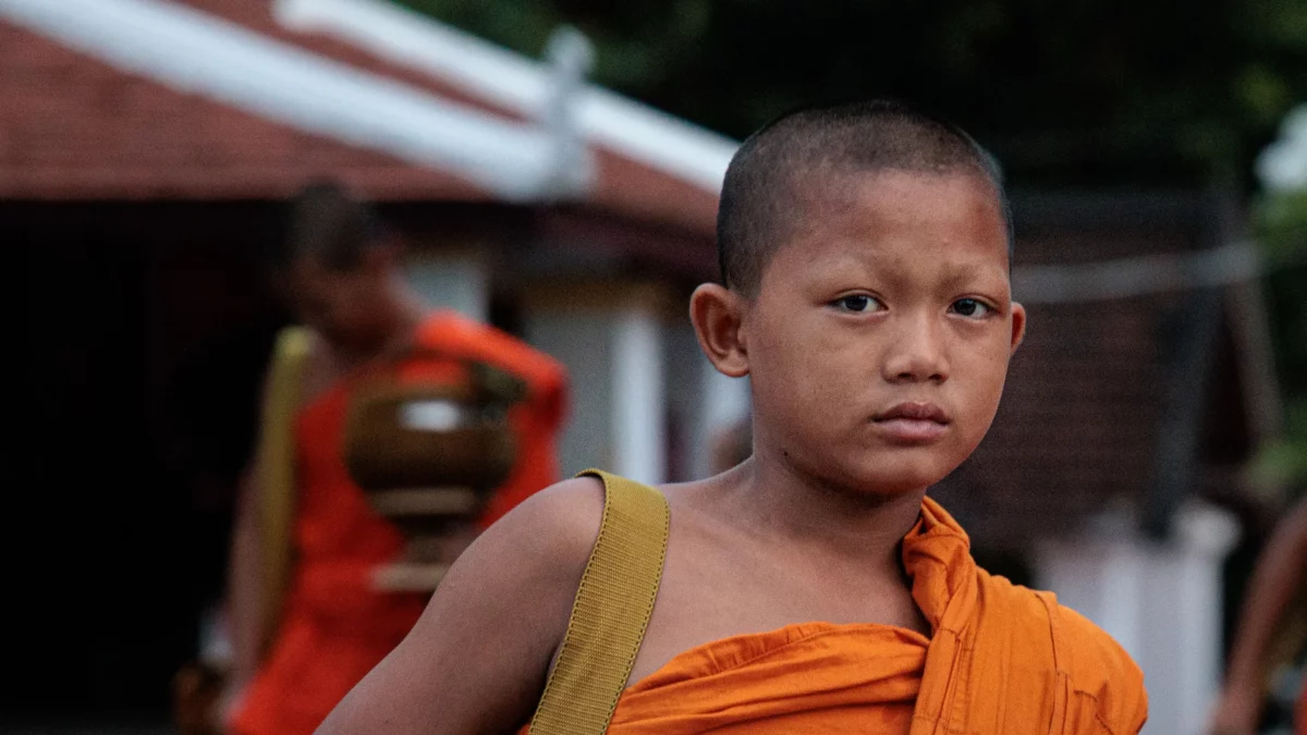 Portrait of a young monk in orange robe, waiting for the alms ceremony to start in Luang Prabang, Laos