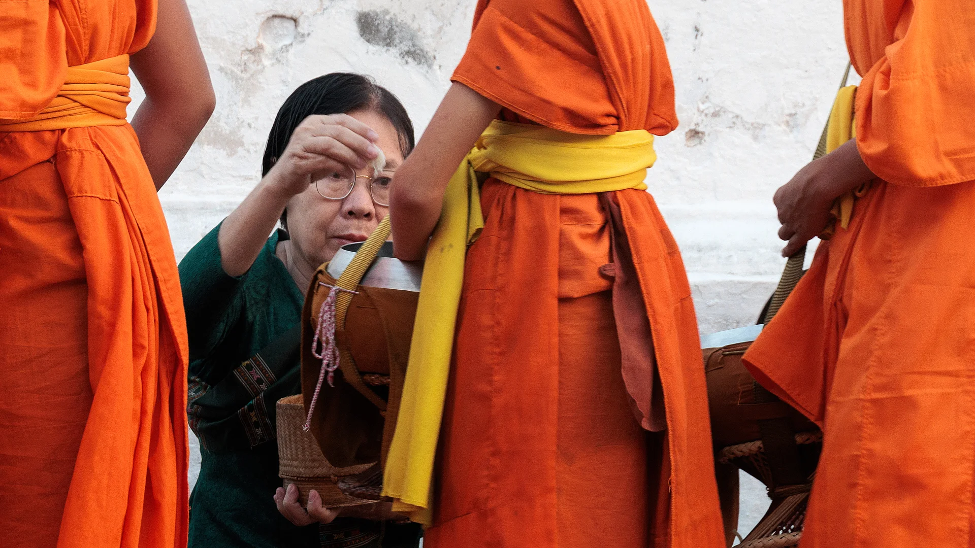 Old women giving food to a young monk at the Alms Ceremony of Luang Prabang in Laos